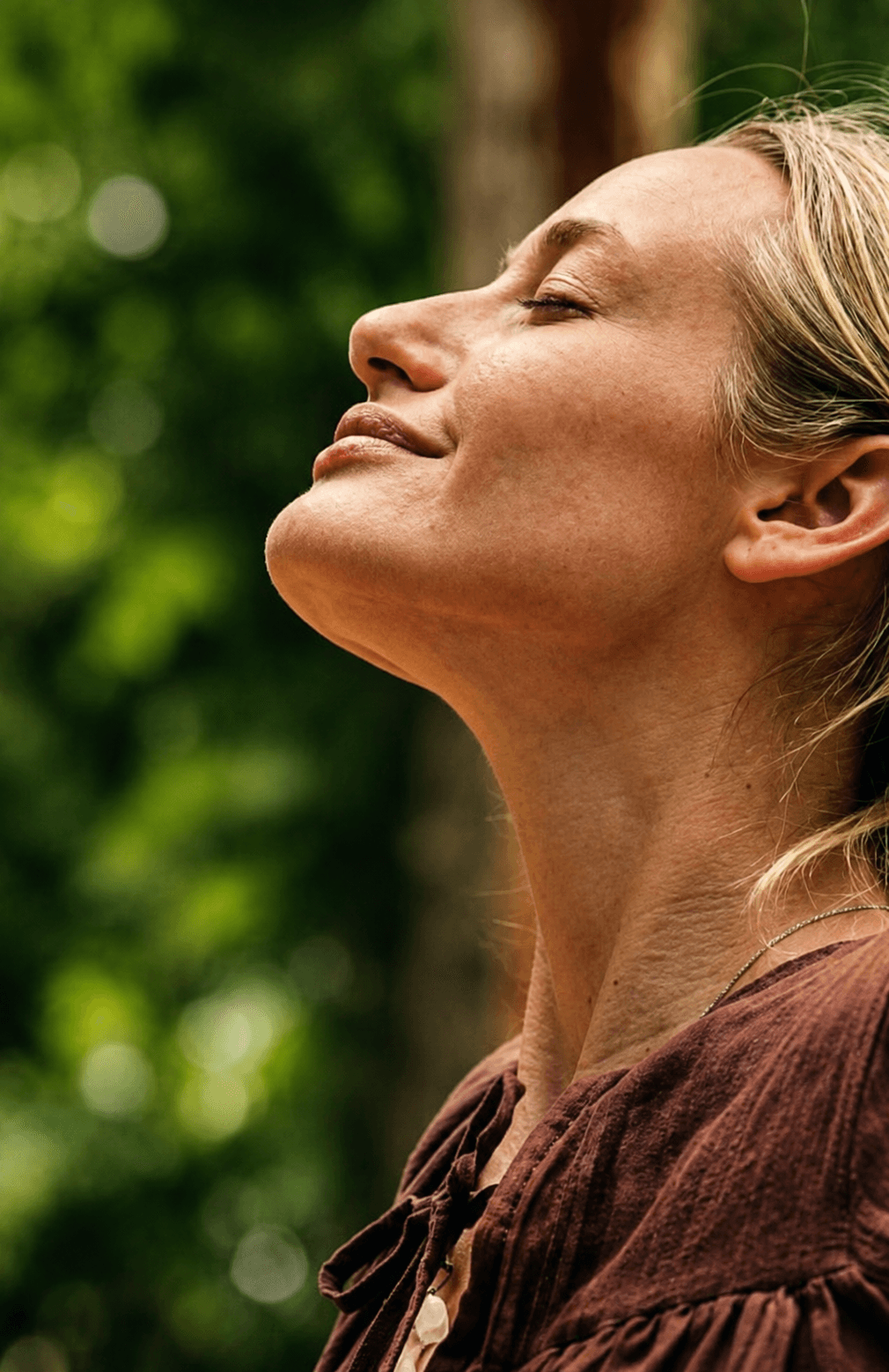 A woman outdoors with her eyes closed, face turned to the light